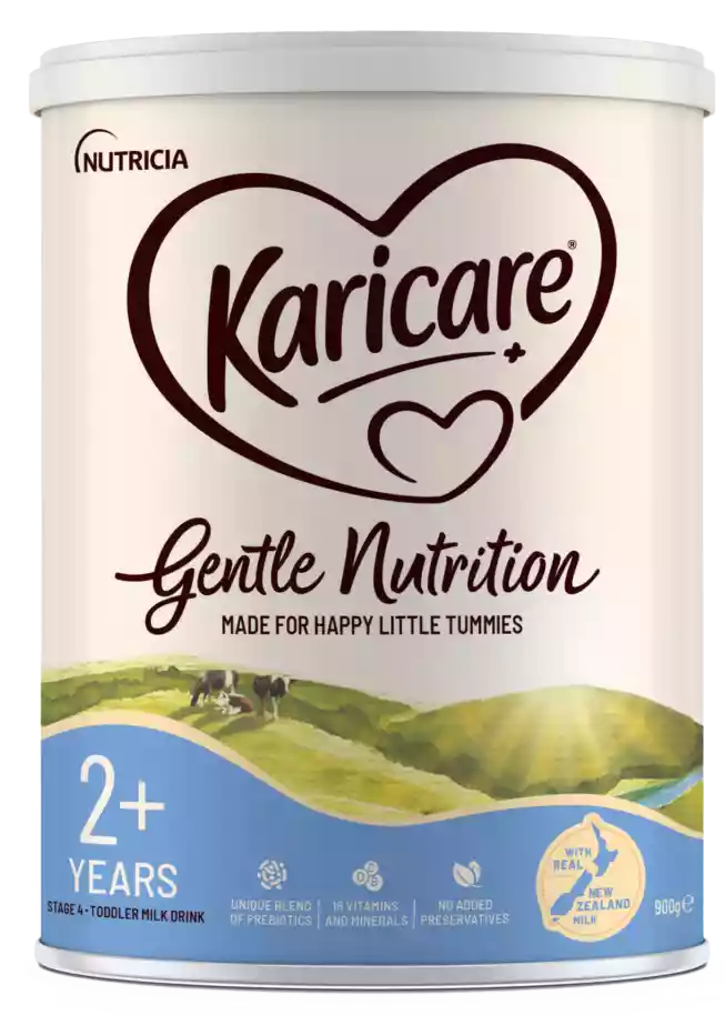 A Karicare Gentle Nutrition toddler milk drink tin is shown against a transparent background. The front label highlights suitability for children aged 2+ years and indicates it is a stage 4 toddler milk drink. The design features a heart-shaped Karicare wordmark, soft cream and blue colors, and an illustrated pastoral landscape with cows and rolling hills. Icons emphasize a unique blend of prebiotics, 18 vitamins and minerals, and no added preservatives, along with a badge stating made with real New Zealand milk and a net weight of 900 g.