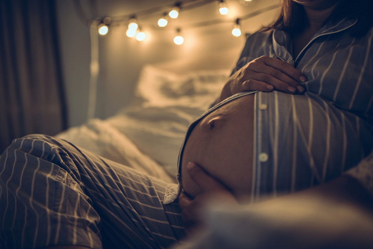 Pregnant woman in bed at home at home holding hands on stomach