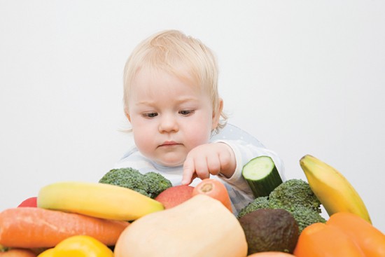 A baby boy looking at a stack of fruit and vegetables