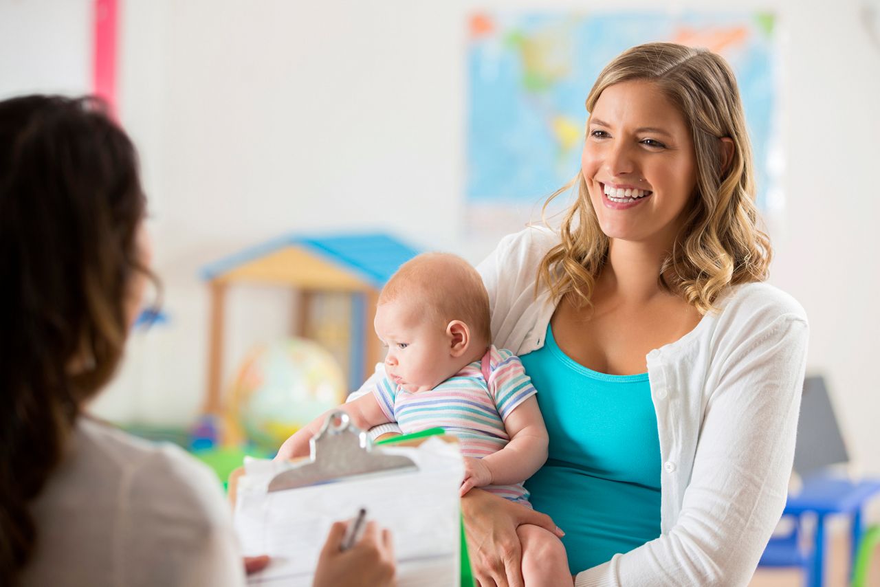 Mae com bebe no colo conversa com professora na creche