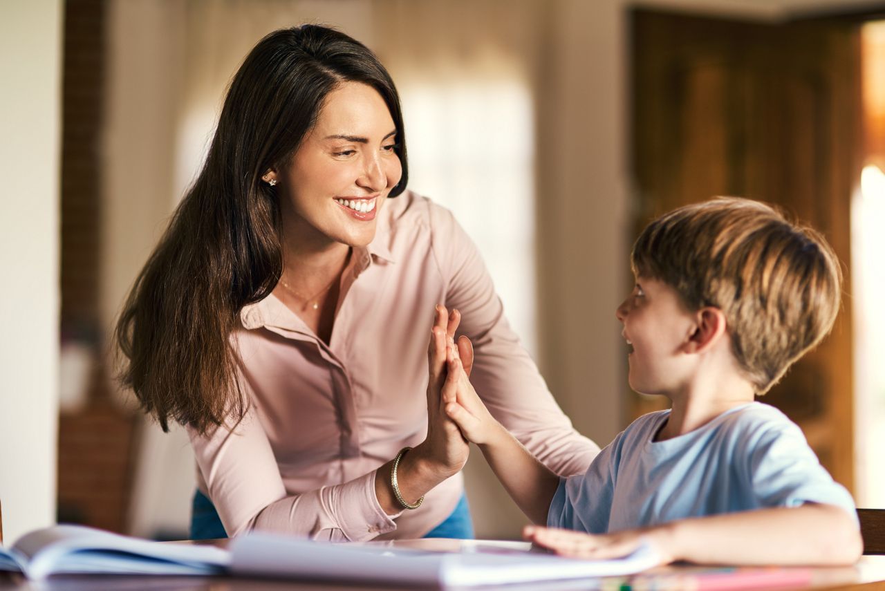 Shot of a mother giving her son a high five while helping him with his homework