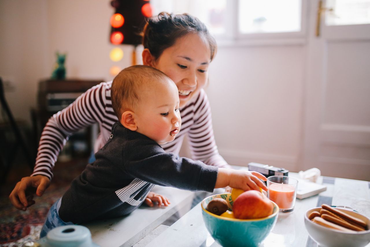 Brightly lit image of a young Thai mom with her little baby boy. They're spending time together at home, playing with toys and having some snacks. Asian family lifestyle concepts, shot in Europe.