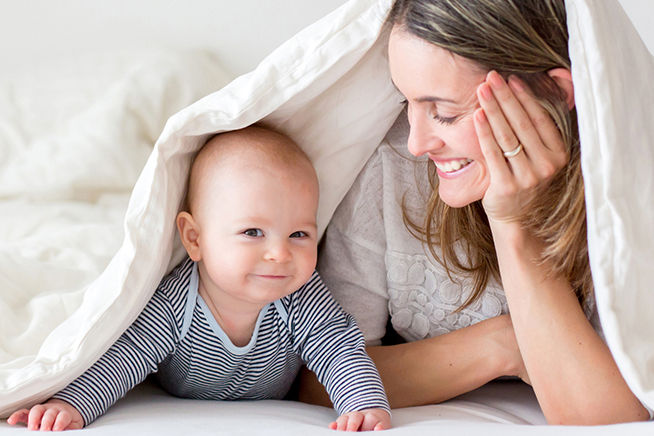 mamá y bebé sonriendo abajo de las cobijas