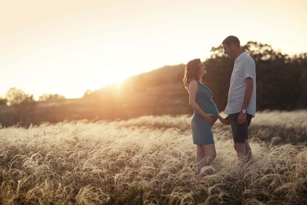 husband and his pregnant wife are walking at sunset in field on the outside. 	 theme  romantic pregnancy outdoors.; Shutterstock ID 141505918,man and pregnant woman walking at sunset