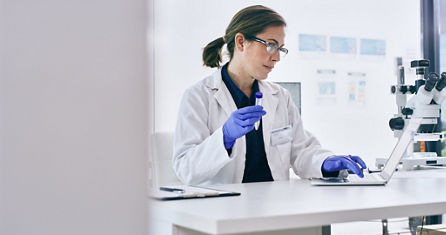 Shot of a young woman analysing samples while working on a laptop in a lab