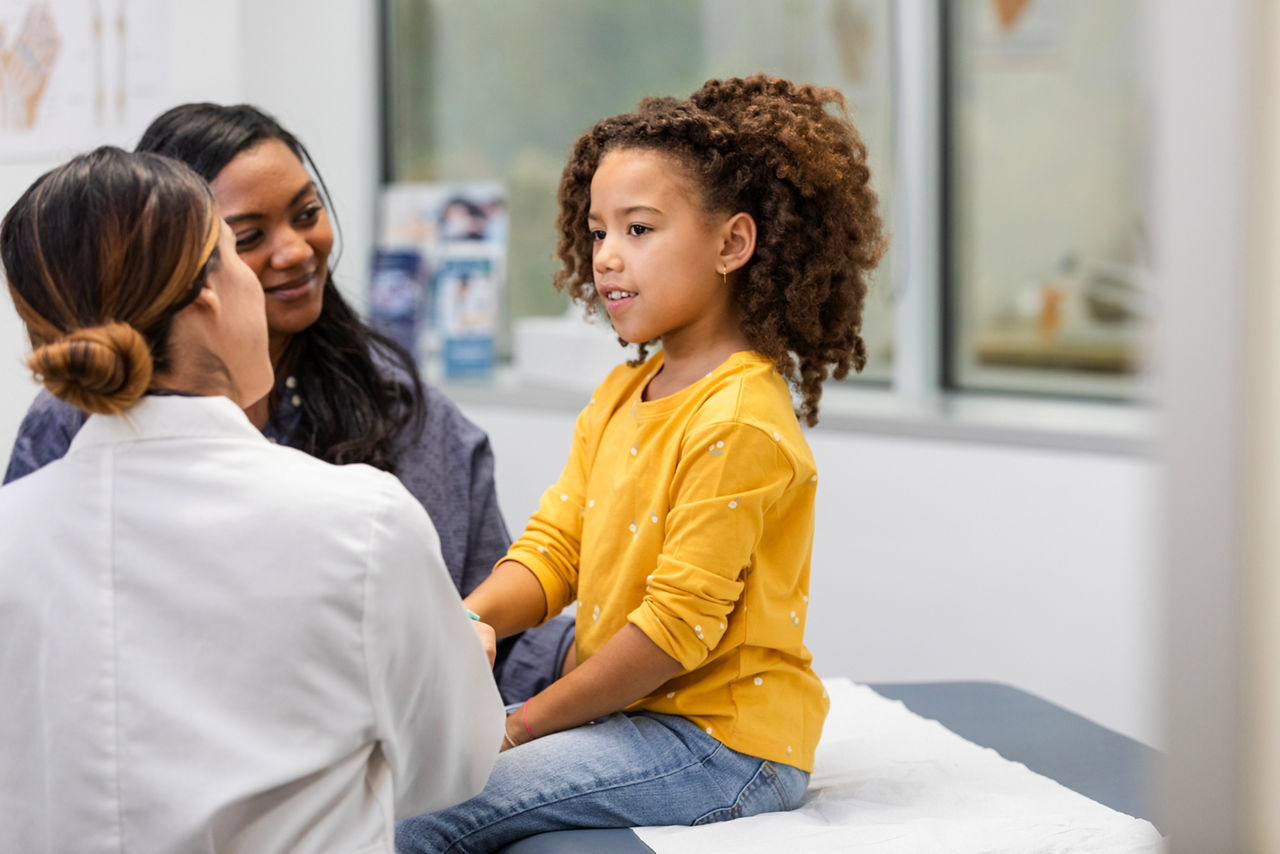 The young female patient smiles while talking to her unrecognizable doctor about her symptoms.