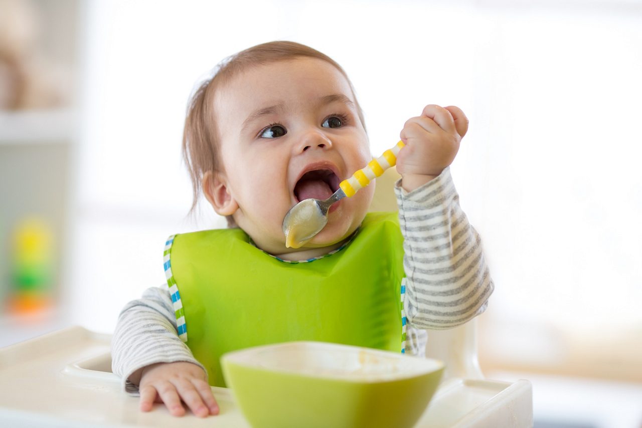 Happy infant baby boy spoon eats itself