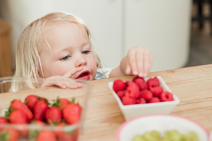 Kleinkind greift nach Himbeeren vom Tisch