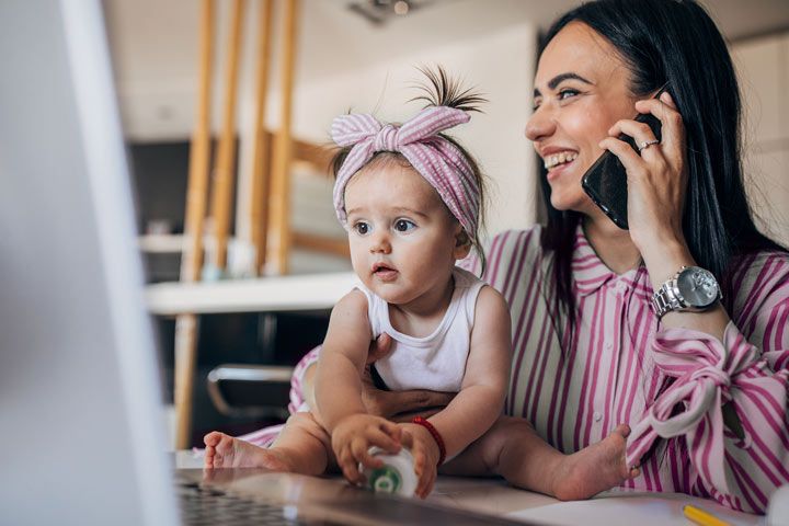 Mutter hält Baby telefonierend vor dem Laptop