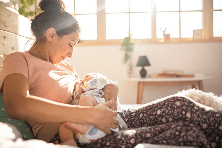 Mutter stillt Baby vor sonnigem Fenster