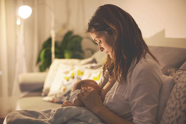 Mutter stillt Baby auf der Couch abends