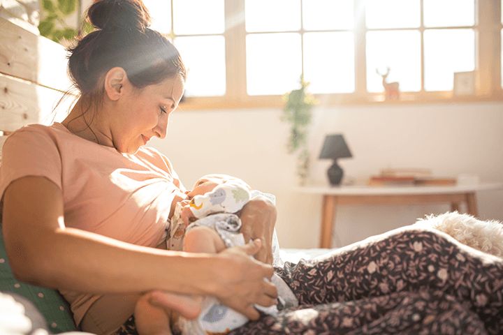 Mutter stillt Baby vor sonnigem Fenster