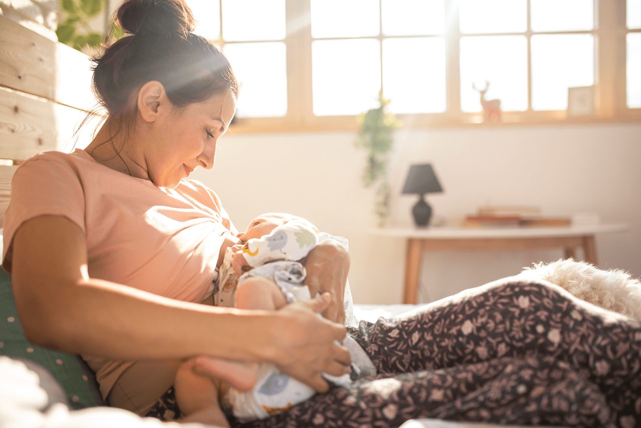 Mutter stillt Baby vor sonnigem Fenster
