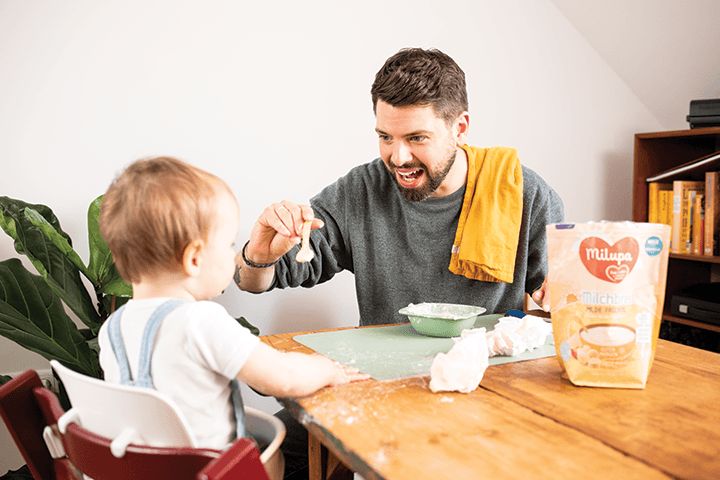 Vater füttert lächelnd Kleinkind mit Brei am Esstisch