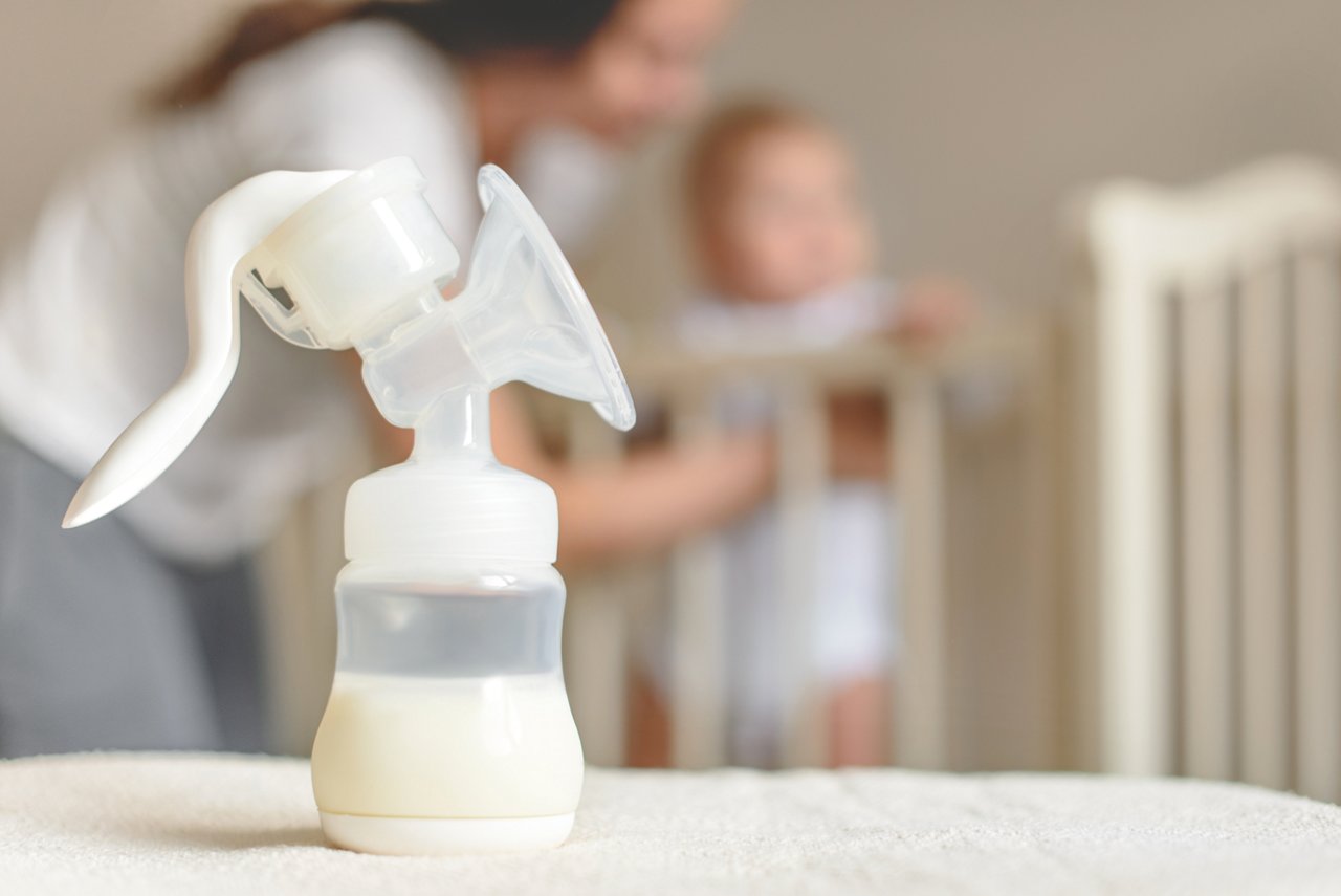 Manual breast pump and bottle with breast milk on the background of mother and baby near the baby's bed. getty images 935281900