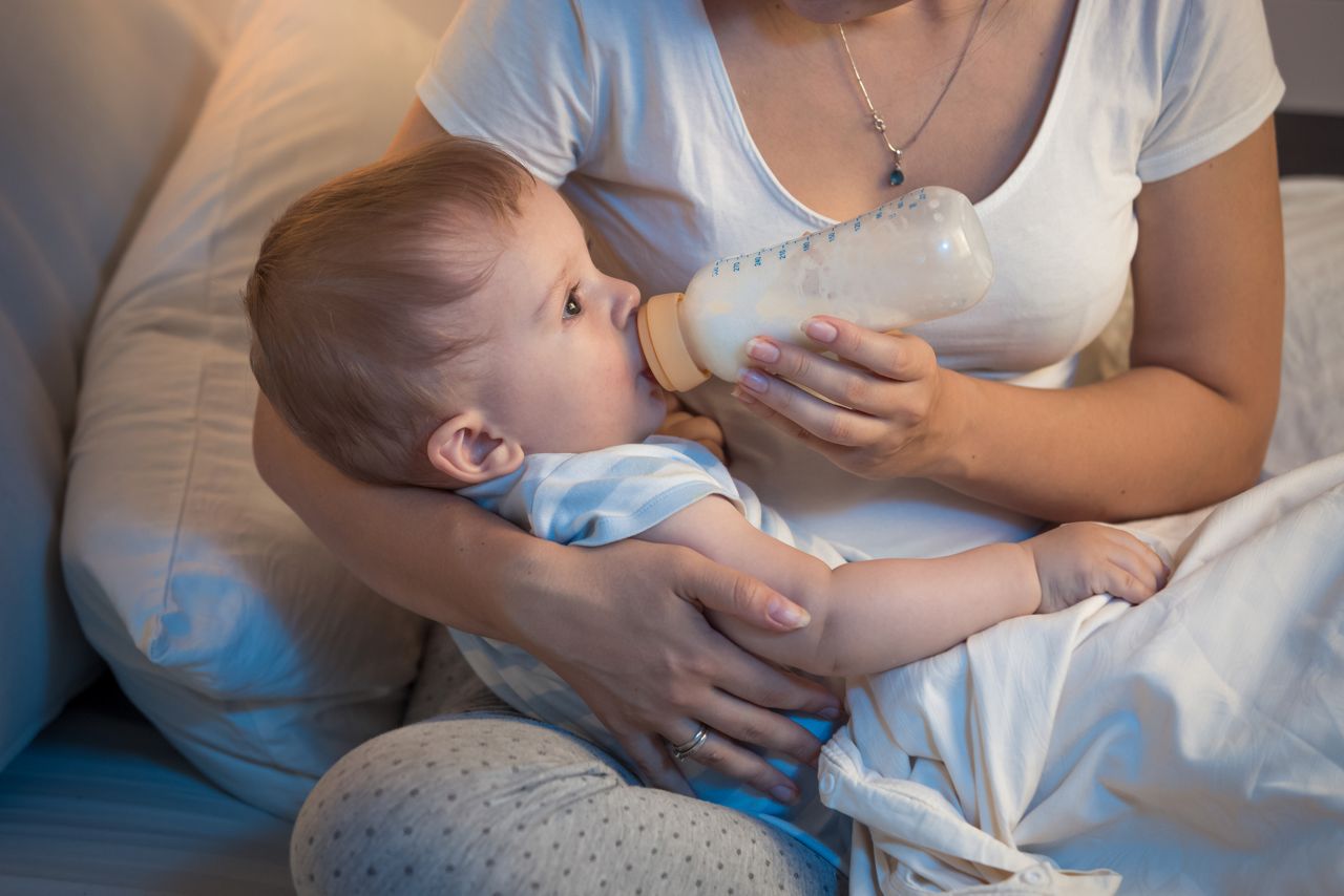 Closeup portrait of beautiful baby boy drinking milk from bottle at night