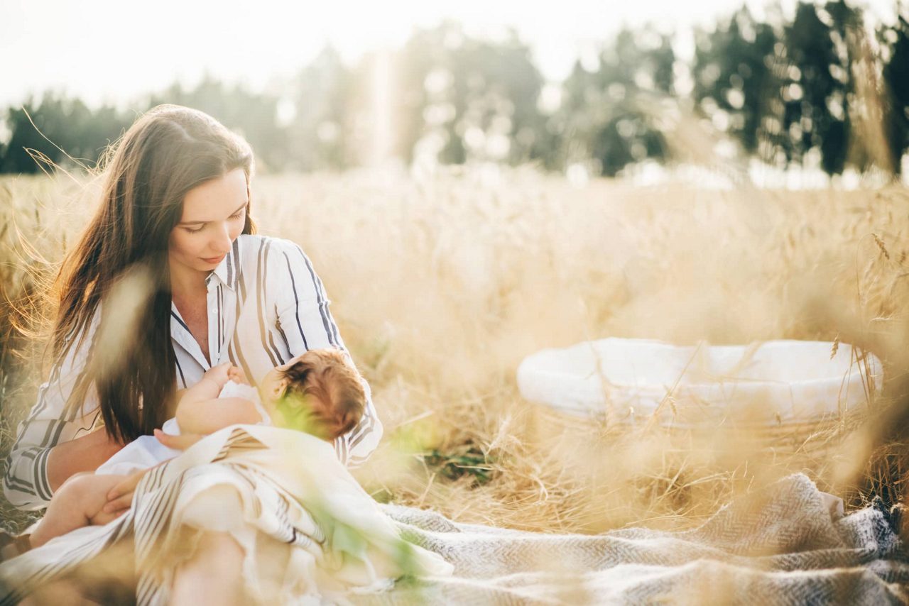 Mutter sitzt in einem Feld und stillt ihr Baby 