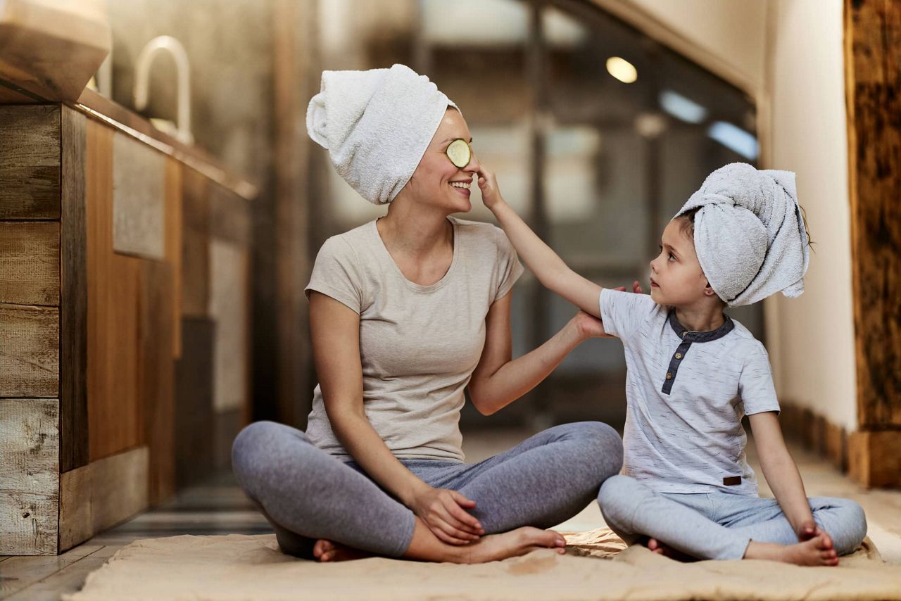 Kind und Mutter sitzen mit Gurken Maske im Schneidersitz