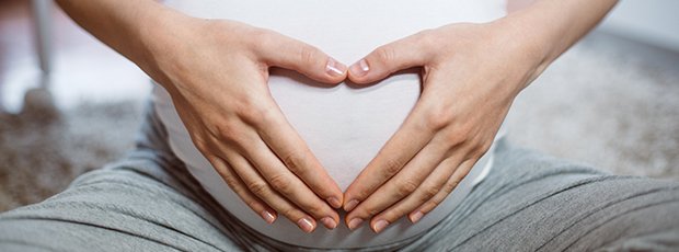 Frau hält ihren Babybauch und zeigt ein Herz