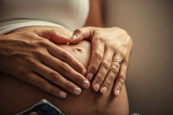 Frau auf Sportmatte hält Babybauch