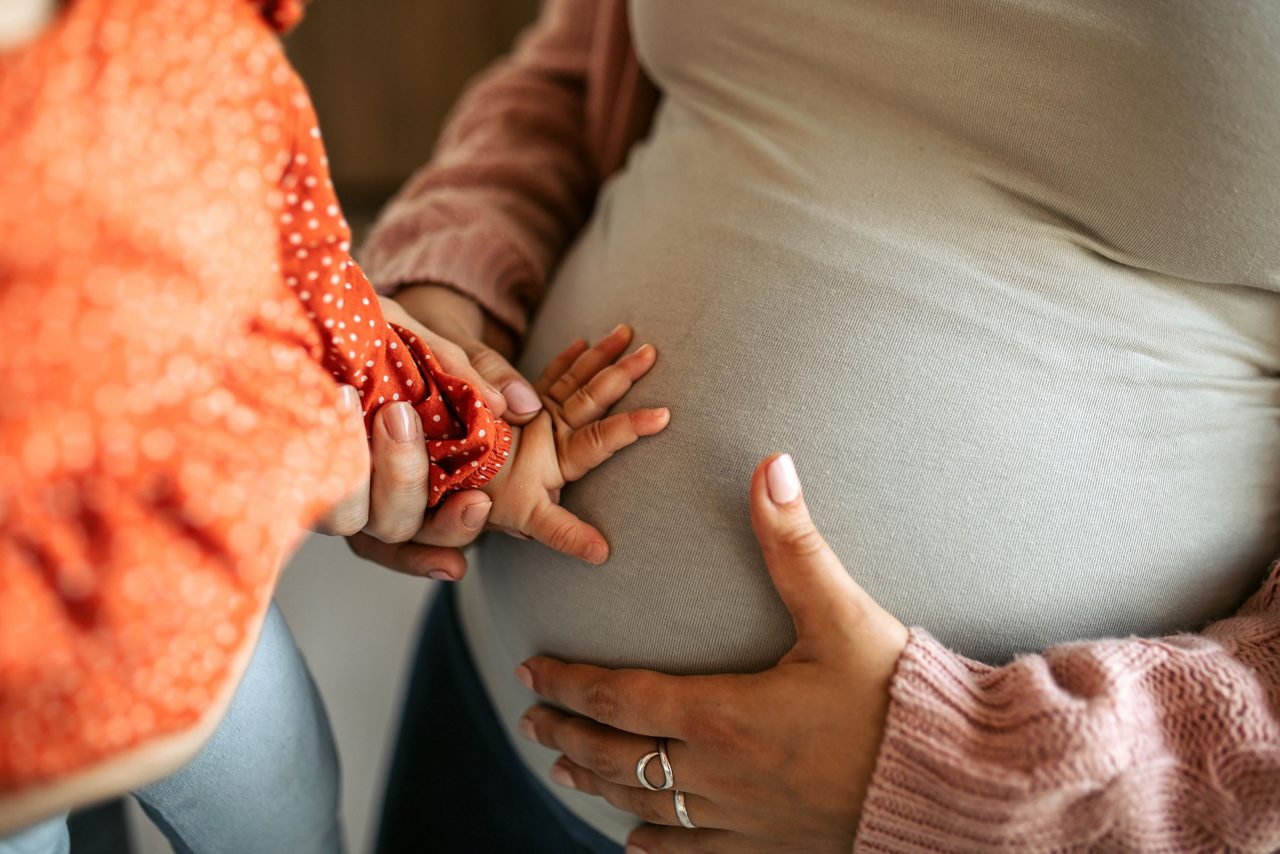 Kind streichelt Babybauch der Mutter