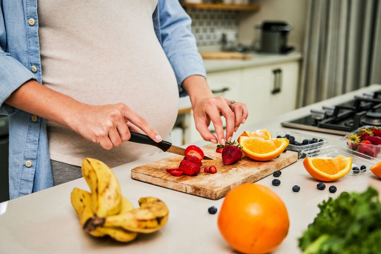 Schwangere steht in der Küche und schneidet Früchte
