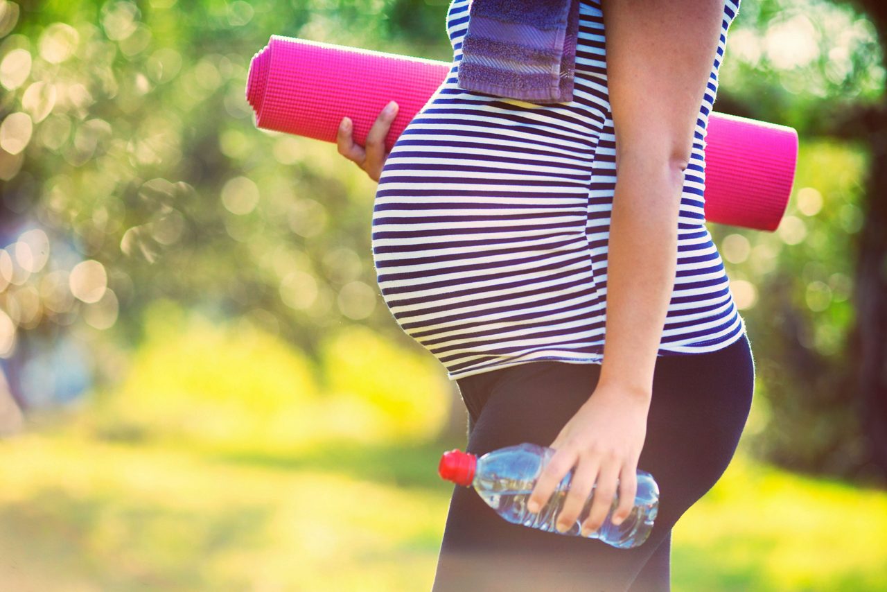 Schwangere Frau mit Yogamatte und Wasserflasche