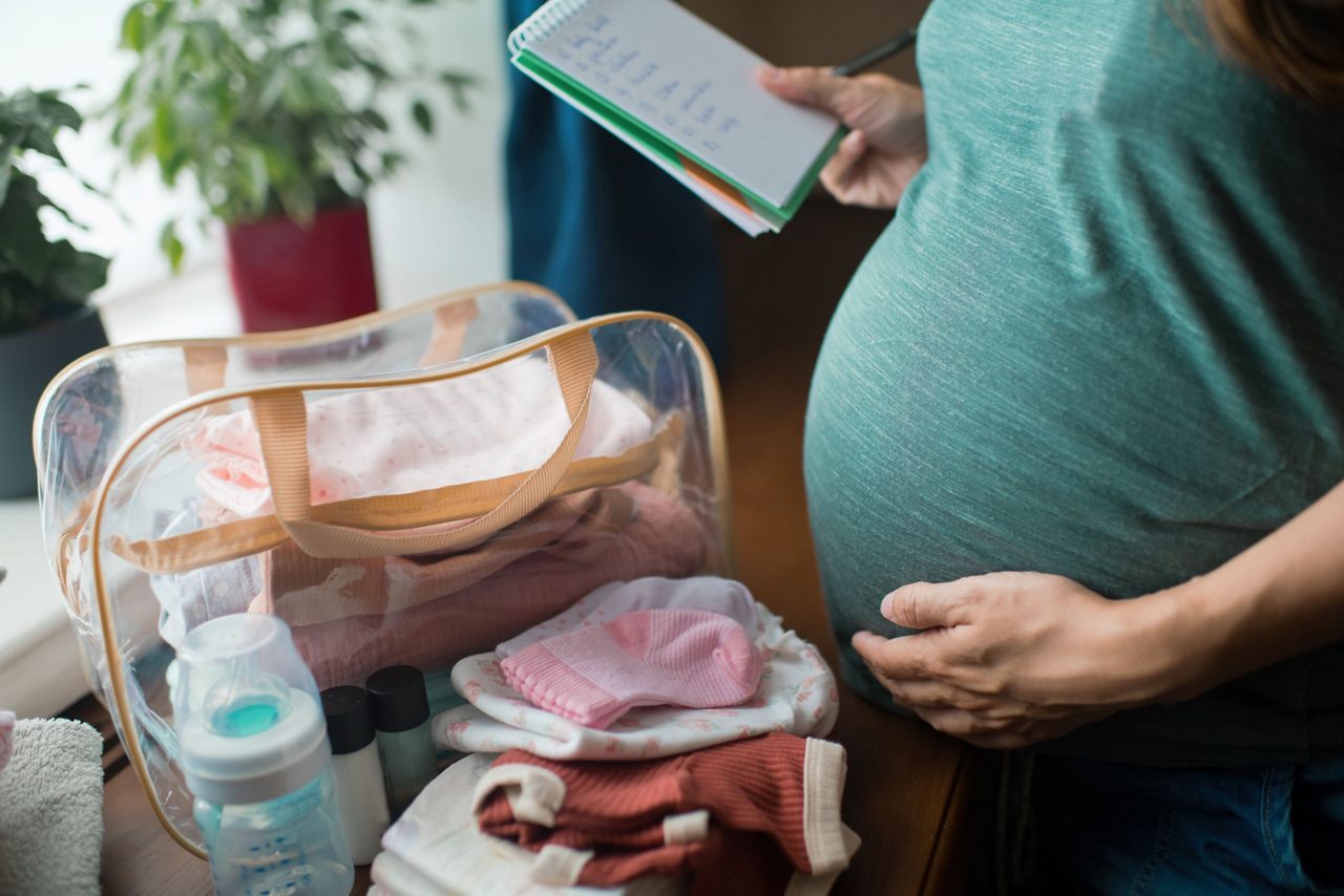 Schwangere Frau mit Kliniktasche und Checkliste