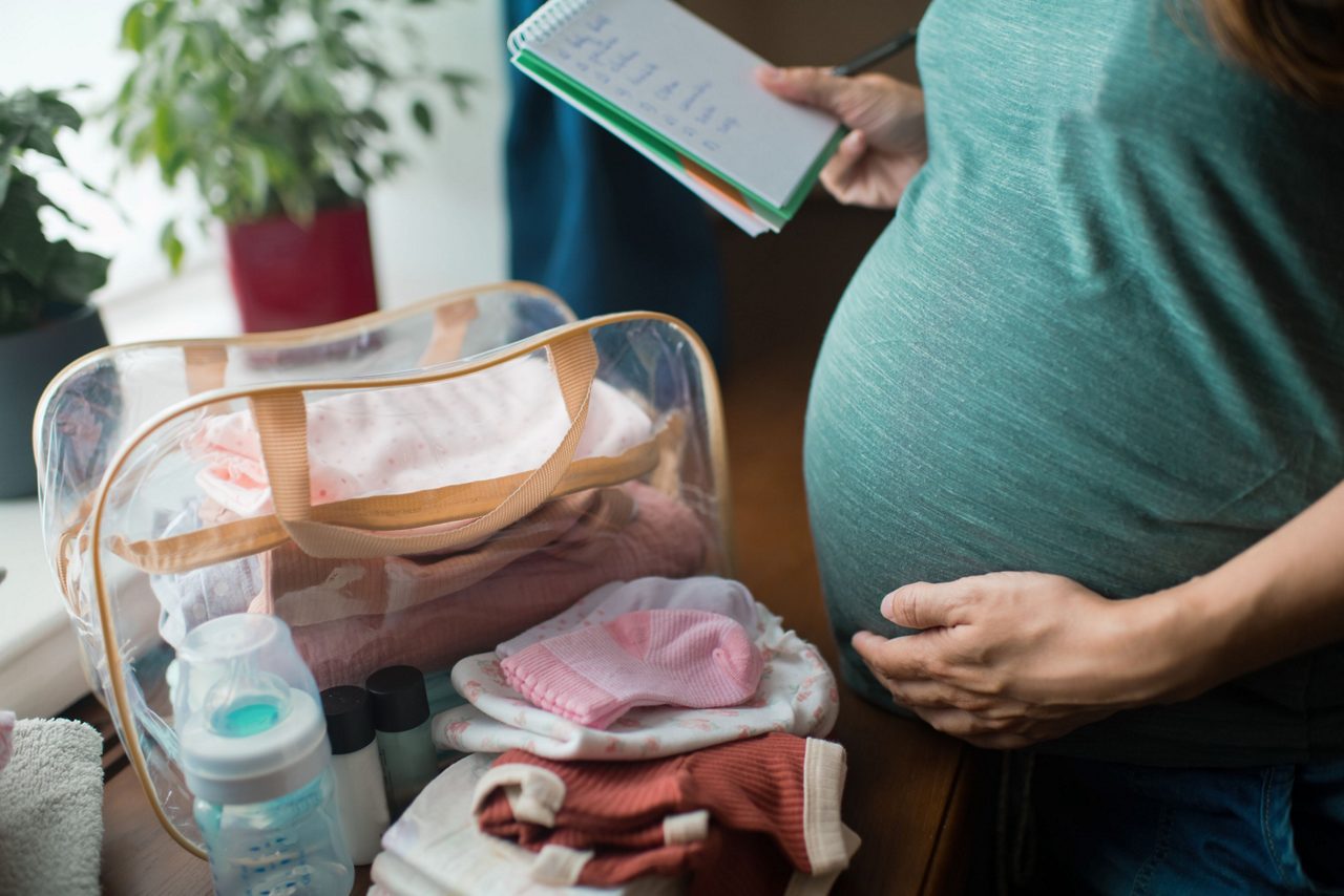 Schwangere Frau mit Babytasche und Checkliste 