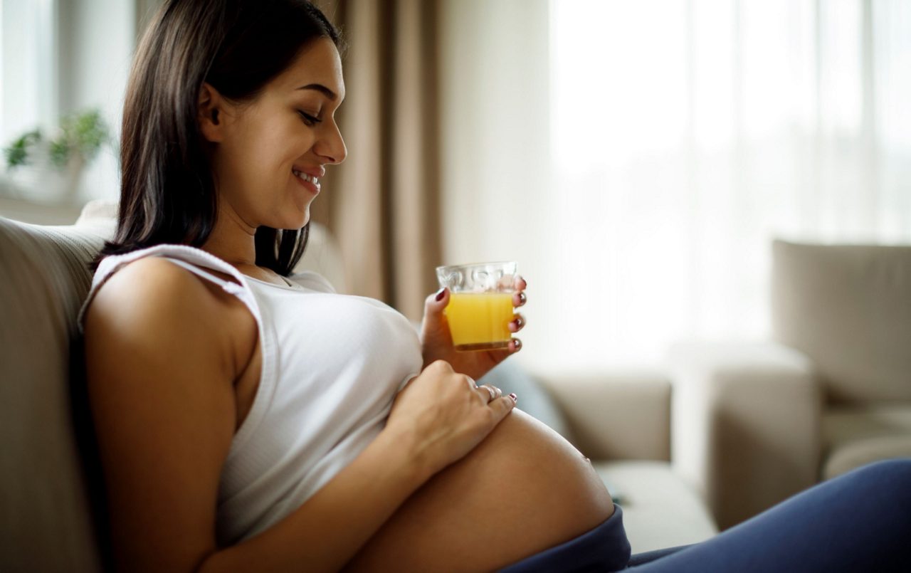Schwangere hält Babybauch und hält Saft in der Hand