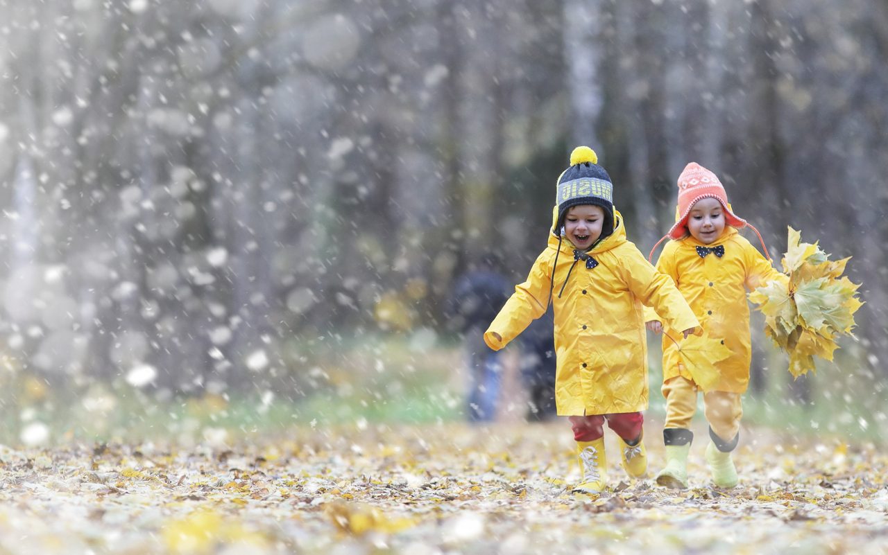 Kleinkinder spielen bei Regen im Laub