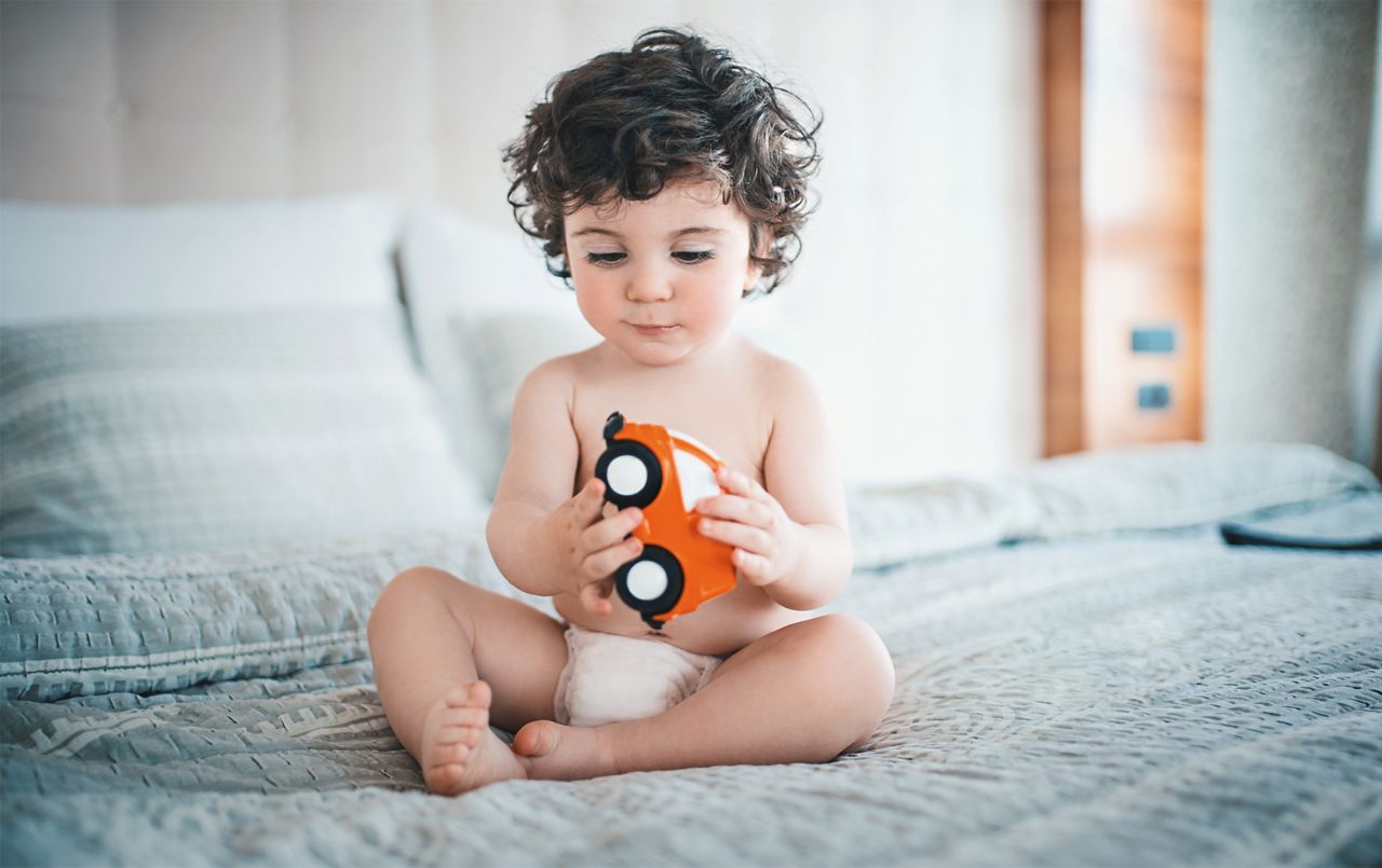 Kleinkind in Windeln spielt mit Spielzeugauto auf dem Bett