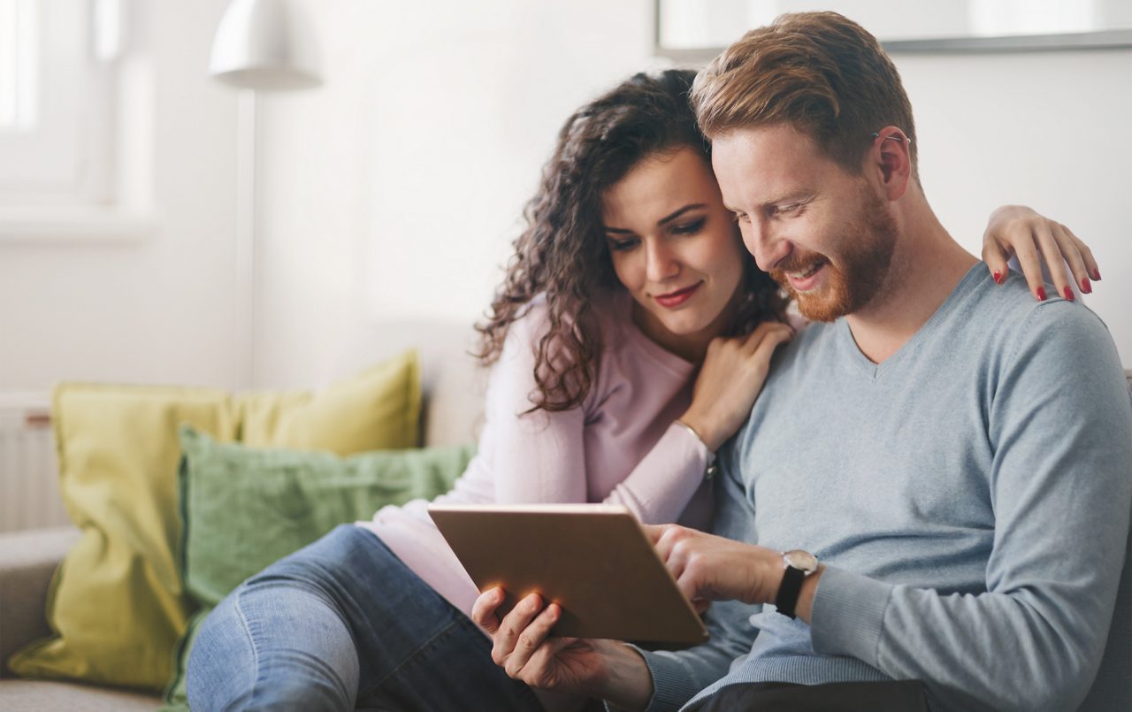 junges Paar sitzen auf der Sofa und schauen auf ein Tablet