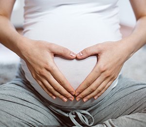 Frau hält ihren Babybauch und zeigt ein Herz