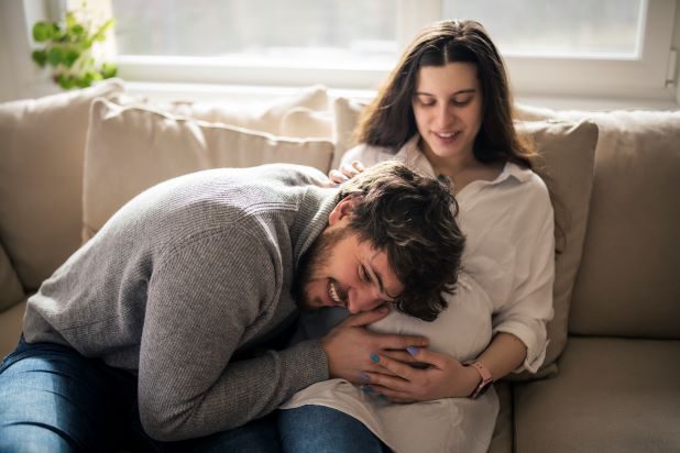 Frau und Mann auf der Couch und lachen und Frau zeigt Ultraschall Foto.