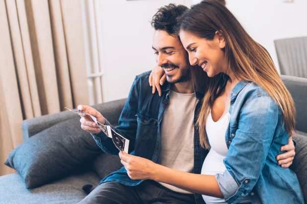 Frau und Mann auf der Couch und lachen und Frau zeigt Ultraschall Foto.