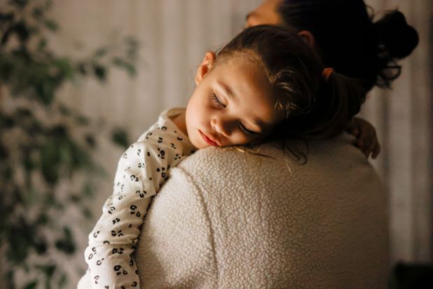 Kleinkind schläft auf Arm der Mutter