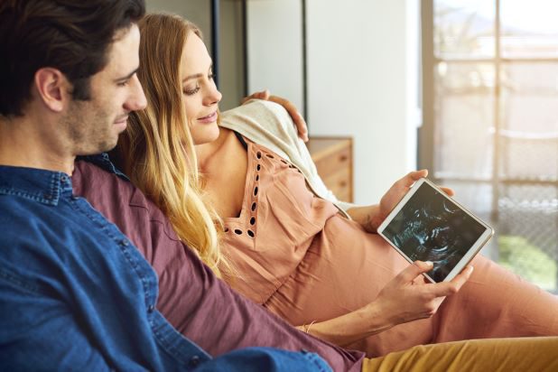 Paar blickt glücklich auf Tablet mit Ultraschallbild