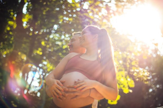 Paar hält Babybauch mit sonnigem Hintergrund