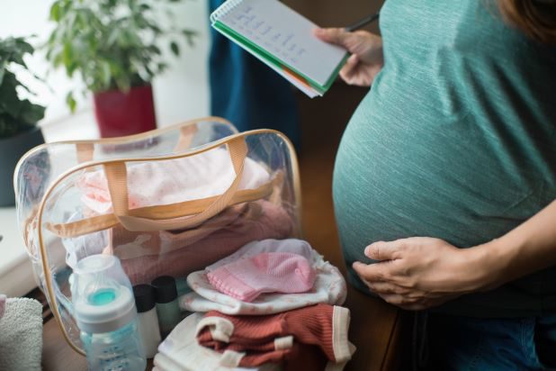 Schwangere hält Bauch und packt Kliniktasche