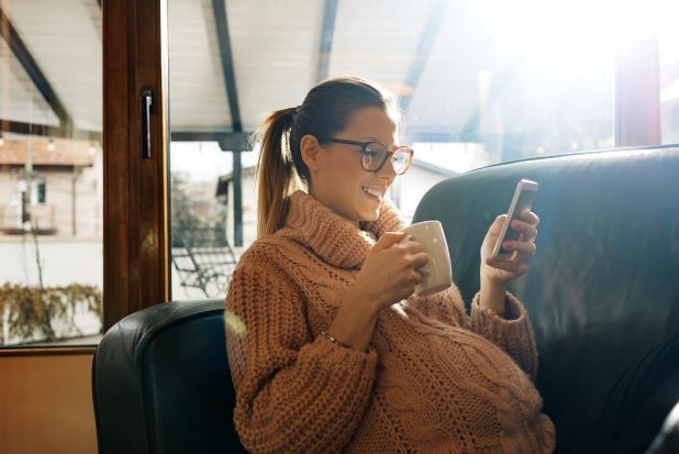 Schwangere mit Handy und Kaffee lächelnd