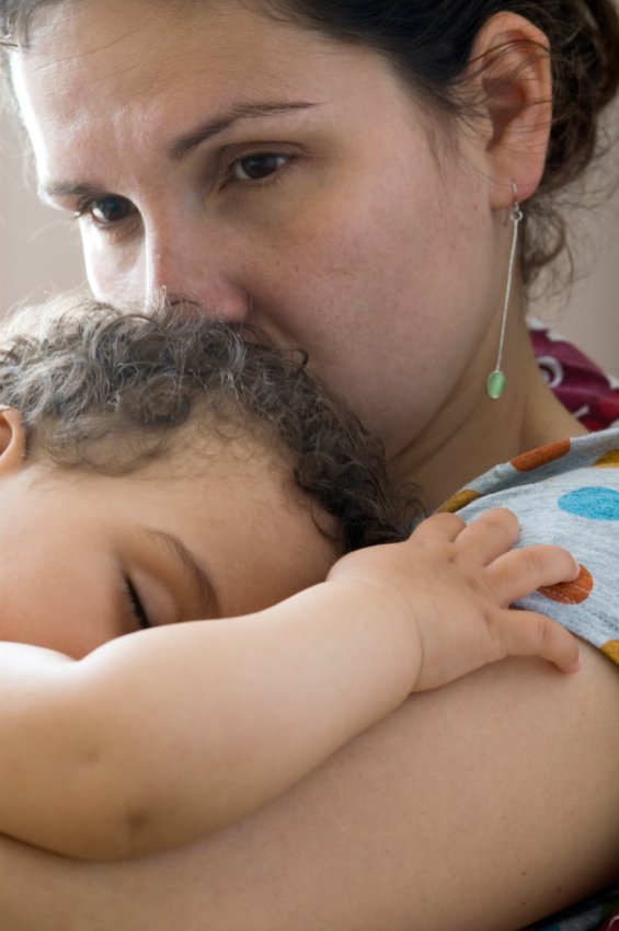 Mother is holding her sleeping baby. She looks concerned and worries