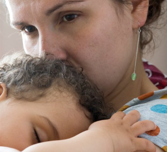 Mother is holding her sleeping baby. She looks concerned and worries