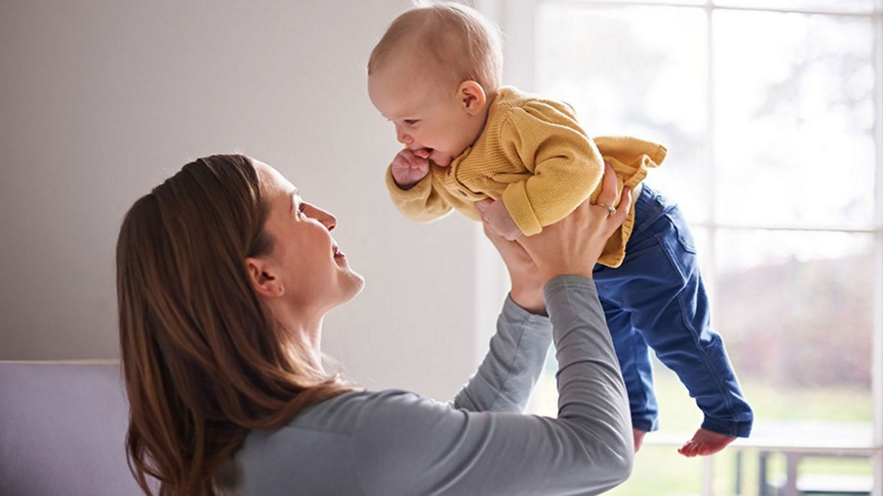 Madre sosteniendo y levantando a su bebé mientras sonríen, fomentando el vínculo emocional y el desarrollo a través de juegos para bebés