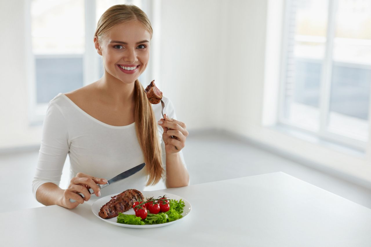 Woman Eating Food. Beautiful Smiling Female Having For Dinner Delicious Grilled Meat With Fresh Vegetables In Kitchen. Healthy Attractive Girl Dining Having Beef Steak With Tomatoes, Salad. Nutrition