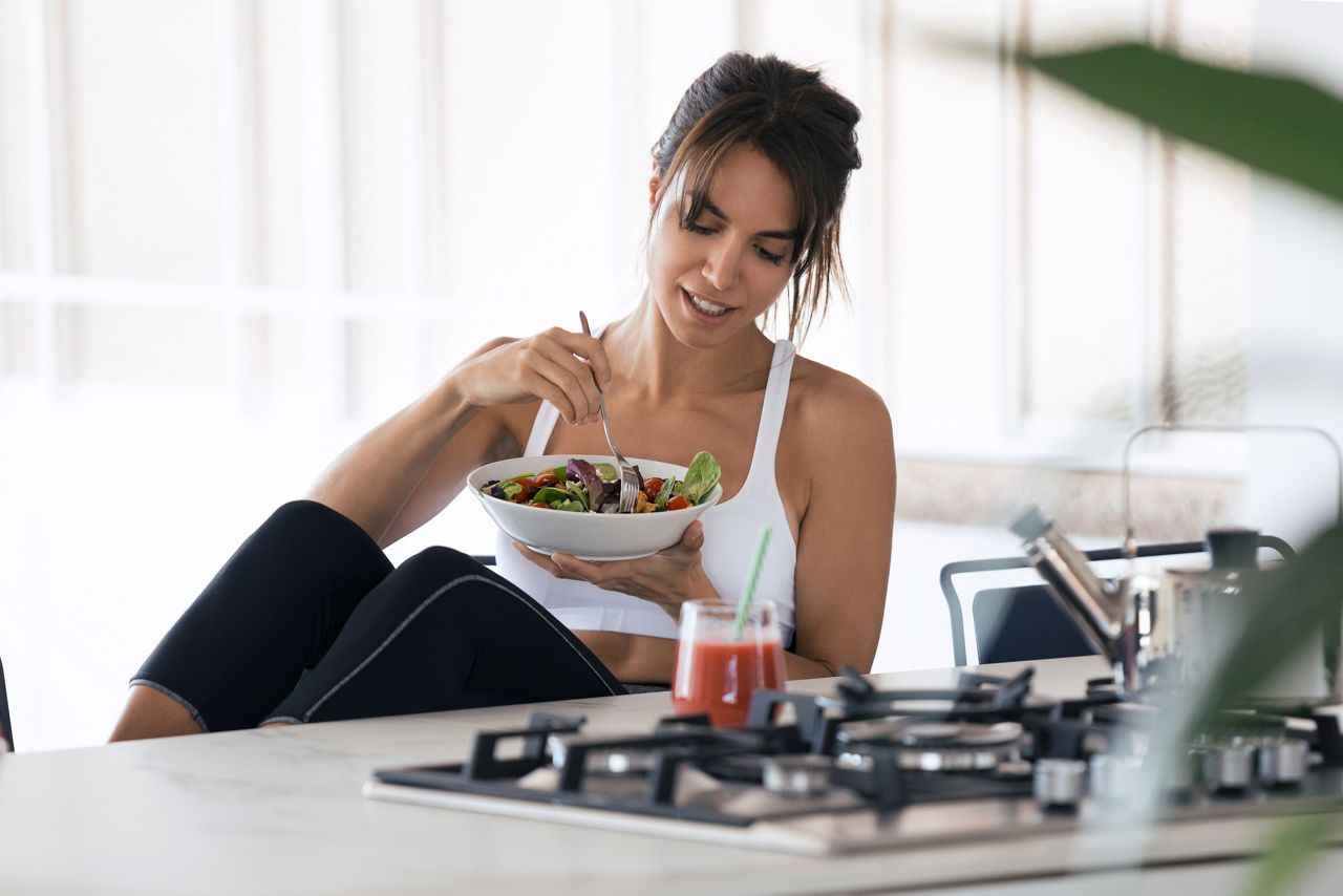 Shot of sporty young woman eating salad and drinking fruit juice in the kitchen at home.