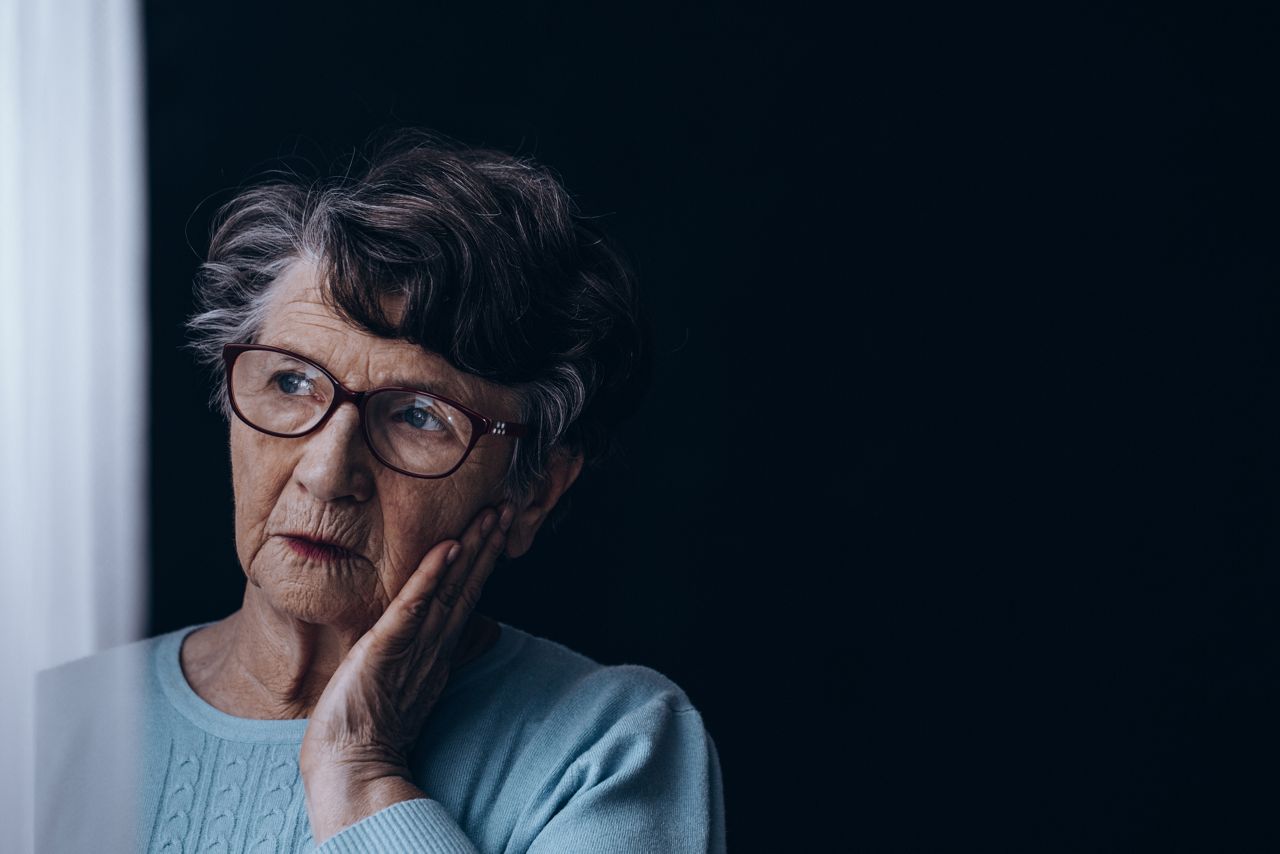Sad, old woman standing alone in dark room