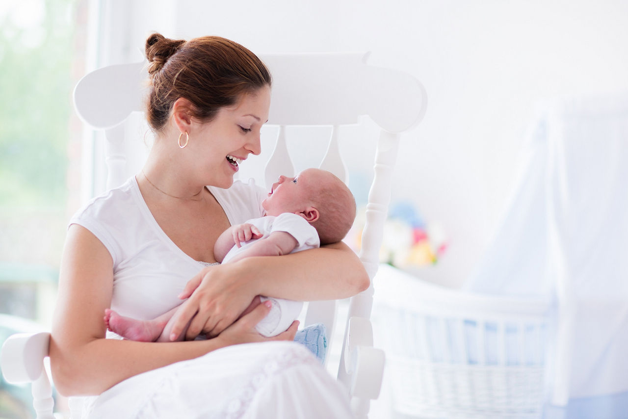 Young mother holding her newborn child. Mom nursing baby. Woman and new born boy relax in a white bedroom with rocking chair and blue crib. Nursery interior. Mother breast feeding baby. Family at home; Shutterstock ID 314288807,mum and baby relaxing in nursery