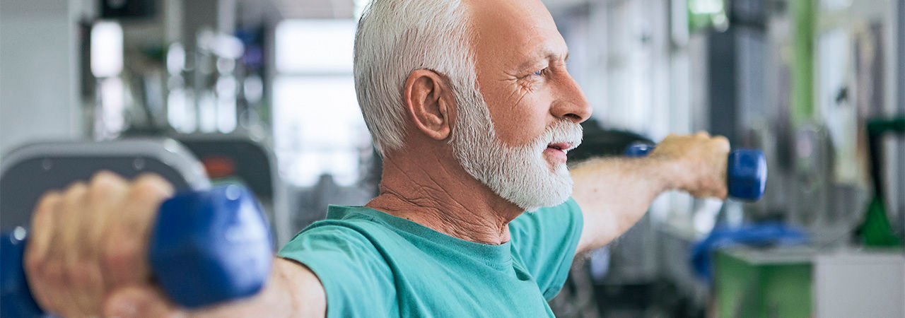 Senior man having strength exercise in gym with weights
