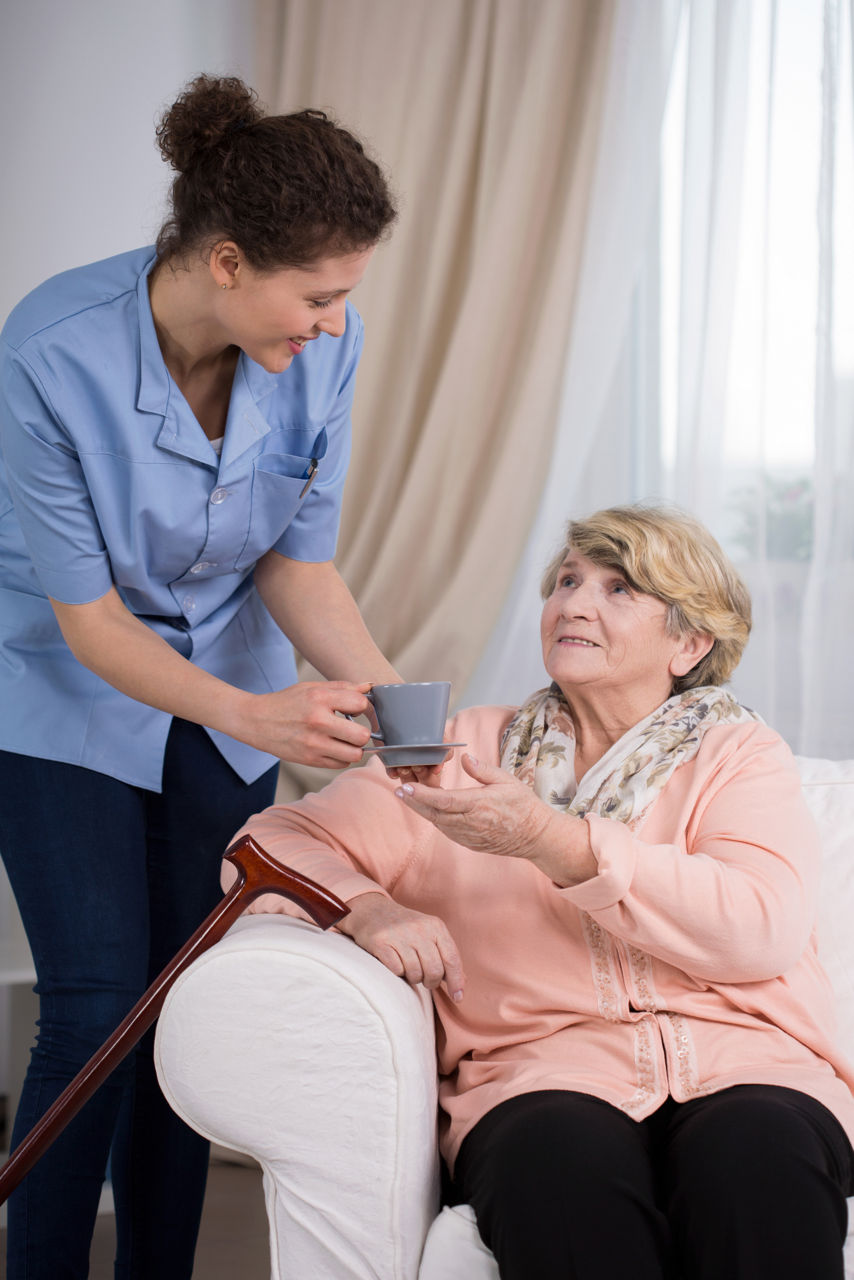 Helpful young caregiver servicing the tea to older lady